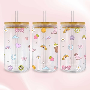 Könnte beinhalten: Drei transparente Gläser in Dosenform mit Bambusdeckeln und Strohhalmen. Jedes Glas hat ein einzigartiges Muster aus bunten Cartoon-Grafiken, darunter Regenbogen, Blumen und Cowboy-Stiefel. Die Gläser sind für kalte Getränke konzipiert.