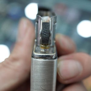 K&ouml;nnte beinhalten: Nahaufnahme eines silbernen Metallfeuerzeugs. Das Feuerzeug hat ein strukturiertes schwarzes Feuersteinrad, einen Docht und ein geb&uuml;rstetes Metallfinish. Das Design ist einfach und funktional, mit Fokus auf die wesentlichen Bestandteile eines Feuerzeugs.