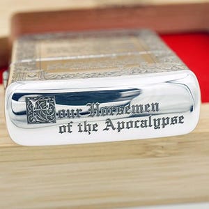 May include: A silver-colored lighter with the words "Our Horsemen of the Apocalypse" engraved on the front. The lighter has an ornate design on the top and is set in a wooden box.