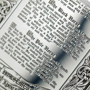 May include: Close-up of a metal plaque with engraved text. The text includes phrases like "The Black Horse" and "The Pale Horse." The design features ornate borders and gothic-style lettering, evoking a historical or fantasy theme.