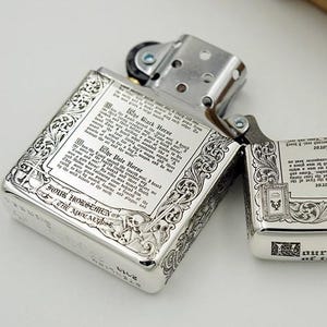 May include: Two silver-colored lighters with intricate engraved designs. One is open, revealing the interior, while the other is closed. The lighters feature detailed text and ornate borders, with the words "FOUR HORSEMEN OF THE APOCALYPSE" visible.