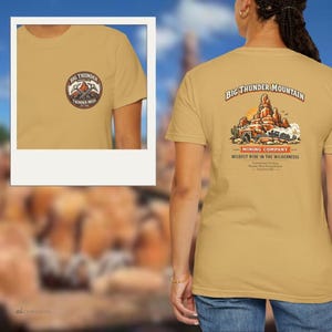 May include: Mustard-coloured t-shirt with a Big Thunder Mountain graphic. The front has a small circular logo with text. The back displays a detailed illustration of the mountain, a mining company logo, and text. A fun tee for theme park enthusiasts.