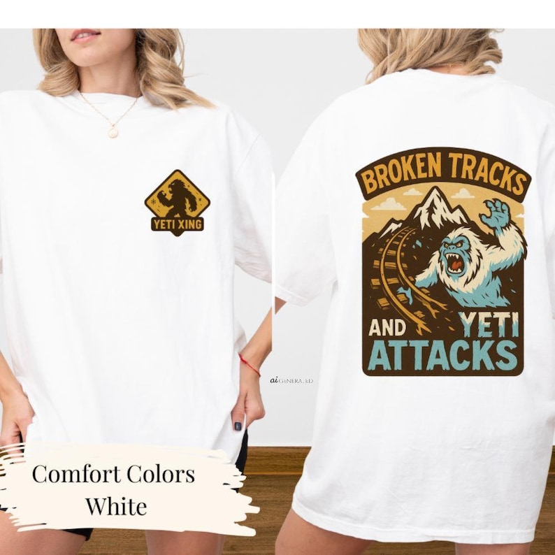 a white t-shirt with a graphic design on the back, depicting a snowy mountain landscape with a large, fierce-looking creature, possibly a Yeti, and the text "Broken Tracks and Yeti Attacks".