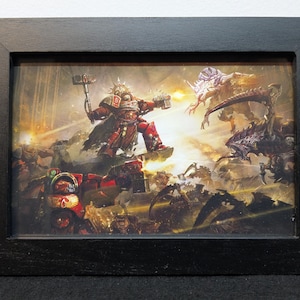 Puede incluir: Obra de arte enmarcada que representa una escena de batalla futurista con un guerrero con armadura roja empuñando un martillo, enfrentándose a criaturas alienígenas. La obra de arte está ambientada en un entorno detallado y lleno de acción, enmarcada en un marco de madera negro.