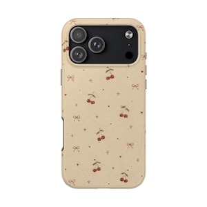 Puede incluir: Una funda de smartphone beige con un patrón repetitivo de pequeñas cerezas rojas, delicados lazos marrones, corazones diminutos y estrellas de cuatro puntas. La funda tiene un módulo de cámara negro con tres lentes y un flash.