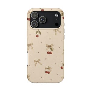 Puede incluir: Una funda para smartphone de color beige con un patrón repetitivo de cerezas rojas con tallos verdes y lazos de color canela claro. El diseño incluye pequeñas formas de corazón dispersas y estrellas de cuatro puntas, con un recorte negro para la cámara.
