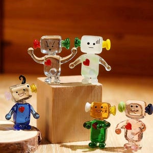 Può includere: Una collezione di figurine di robot in vetro colorato. Ogni robot ha una testa quadrata con accessori a forma di orecchio di diversi colori e un dettaglio a forma di cuore sul petto. I robot sono in vari colori, tra cui trasparente, blu, verde e rosa.
