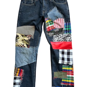 May include: Dark wash denim jeans with multiple fabric patches in various colors and patterns. Patches include floral, plaid, and solid colors. The jeans have a classic five-pocket design and a straight leg fit.