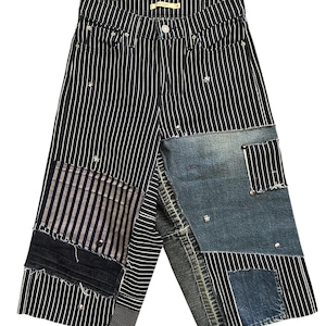 May include: High-waisted jeans in a black and white pinstripe pattern featuring a patchwork design. The garment includes various denim patches in blue and black, frayed edges, and scattered metallic studs throughout the front panels.