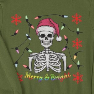 May include: An olive green sweatshirt featuring a skeleton wearing a Santa hat, decorated with Christmas lights and snowflakes. The text "Merry & Brian" is below. Surrounded by gifts, decorations, and a Christmas stocking.