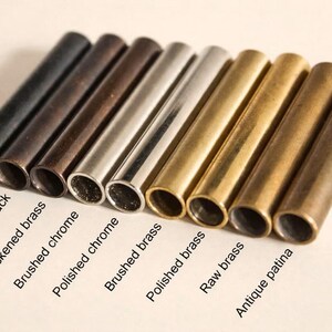 May include: An assortment of cylindrical metal tubes in various finishes, including matte black, antique black, and brushed chrome. The tubes are labeled with their respective finishes, such as "Raw brass" and "Antique patina".