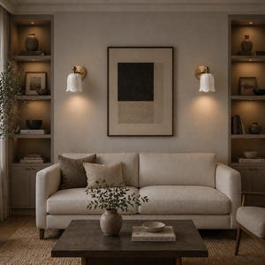 May include: A neutral-toned living room with a cream-colored sofa, decorative pillows, and a dark wood coffee table. Two wall sconces with white tulip-shaped shades flank a framed abstract artwork. Built-in shelves display decor.