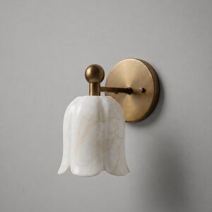 May include: A wall sconce with a white, tulip-shaped shade featuring a marble-like pattern. The sconce has a brass-colored base and a round backplate. The fixture is designed for indoor lighting.