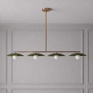 Op de afbeelding: Een moderne, lineaire kroonluchter met vier lampen. De armatuur heeft een messing afwerking en olijfgroene kappen. Elke kap heeft een witte, bolvormige gloeilamp. De kroonluchter wordt door een messing staaf aan het plafond gehangen.