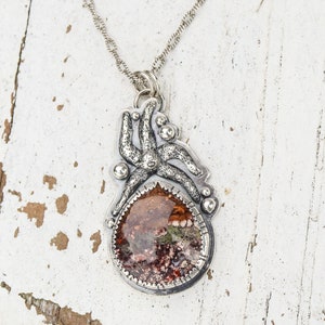 May include: A silver necklace with a pendant featuring a detailed octopus design with a red, green, and brown stone in the center.
