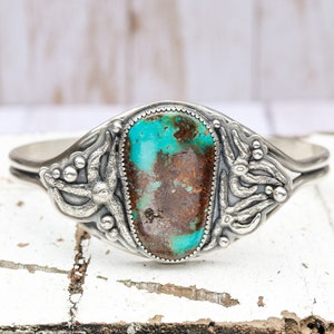 May include: A silver bracelet with a turquoise stone set in a floral design.