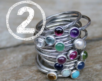 May include: A stack of silver rings with colorful gemstones. The rings are stacked on top of each other, with the gemstones facing outwards. The gemstones are a variety of colors, including red, purple, green, blue, and white.