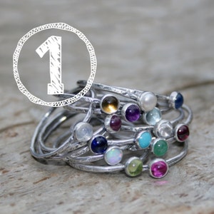 May include: A stack of silver rings with colorful gemstones. The rings are stacked on top of each other, and the gemstones are visible. The gemstones are in a variety of colors, including blue, green, red, purple, and yellow.