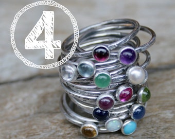 May include: Stack of ten silver rings with colorful gemstones. Each ring has a different colored gemstone, including amethyst, aquamarine, emerald, ruby, sapphire, topaz, and opal.
