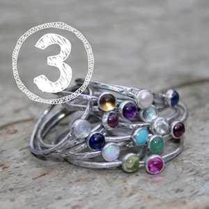 May include: A stack of silver rings with colorful gemstones. The rings are stacked on top of each other, and the gemstones are visible. The gemstones are in a variety of colors, including red, blue, green, and purple.