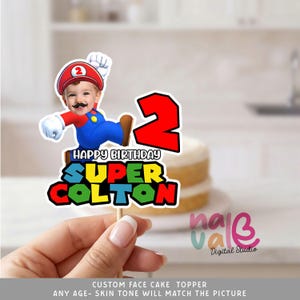Puede incluir: Un adorno para tarta personalizado con el tema de Super Mario Bros., con la cara de un niño. Incluye el número 2 rojo, el texto "Happy Birthday Super Colton" y una imagen de Mario. El adorno está sujeto a un palillo de madera.