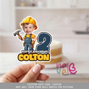 May include: A cake topper featuring a cartoon illustration of a young boy dressed as a construction worker, holding a hammer. The topper includes the number 2, the text "HAPPY BIRTHDAY COLTON", and is held by a wooden stick. The background is blurred.