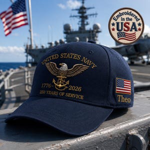 May include: A navy blue baseball cap featuring gold embroidery of the United States Navy eagle and anchor emblem, the text 1776-2026 250 YEARS OF SERVICE, a small American flag patch on the side, and the name Theo embroidered in gold thread below it.