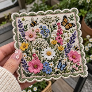 May include: A square fabric patch with a scalloped green border featuring intricate embroidery of a wildflower meadow. The design includes pink, yellow, blue, and white flowers, two bees, and two butterflies, one orange and one blue.