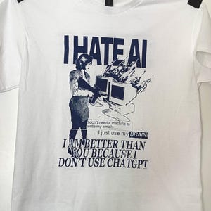 May include: A white short-sleeved t-shirt featuring a dark blue graphic print. The design shows a person holding a rifle near a burning computer with the text: I HATE AI, I don't need a machine to write my emails... I just use my BRAIN, I AM BETTER THAN YOU BECAUSE I DON'T USE CHATGPT.