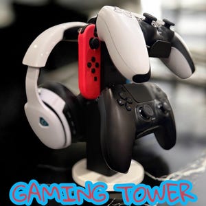 May include: Black and white gaming tower holding a white headset, a red controller, and three game controllers. The text "GAMING TOWER" is written in blue and red.