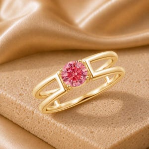 Peut inclure: Une bague en or ornée d'une pierre précieuse rose ronde et facettée au centre. L'anneau présente une conception fendue, où deux barres d'or parallèles s'étendent depuis le sertissage central pour former le corps de la bague.