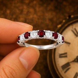 May include: A silver-toned band ring featuring an alternating pattern of round-cut deep red rubies and clear white diamonds set in a prong setting. The ring displays a total of nine stones arranged horizontally across the top of the metal band.