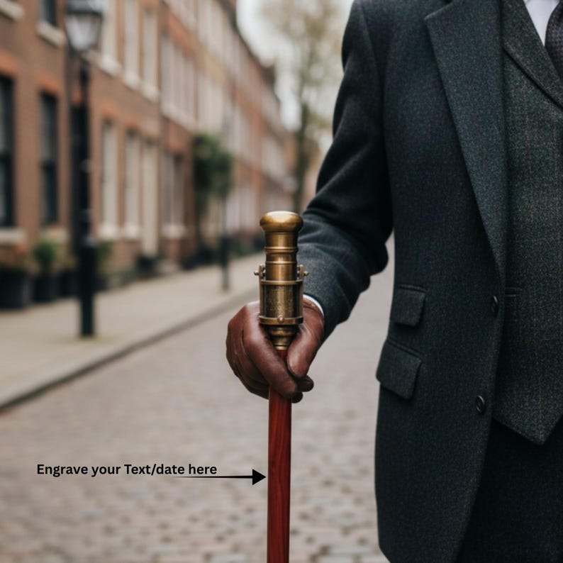 May include: A vintage-style walking cane with a brass handle and a dark red wooden shaft. The cane is held by a person wearing a dark gray suit. The text "Engrave your Text/date here" is visible.