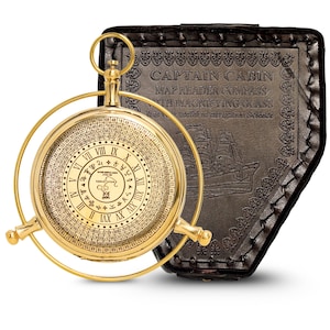 May include: A gold-colored Captain Cabin map reader compass with a magnifying glass. The compass features Roman numerals and a circular scale. It is housed in a black leather case with embossed text and a ship illustration.