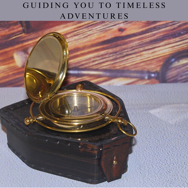 May include: A vintage brass compass with a hinged lid, resting on a dark brown leather case. The compass is open, revealing the internal dial. The text "GUIDING YOU TO TIMELESS ADVENTURES" is at the top of the image.
