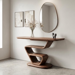 May include: A dark wood console table with a continuous, serpentine-shaped base and a flat rectangular top. The table features a smooth, polished finish and a sculptural design. It is positioned against a wall with a mirror and two framed prints.