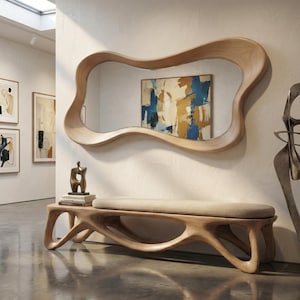 May include: A large wall mirror with an irregular, organic wooden frame featuring a light brown grain. Below it sits a matching wooden bench with a long, beige upholstered seat cushion and a fluid, sculptural base with open cutouts.