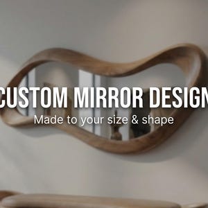 May include: A custom mirror design with a unique, flowing wooden frame. The mirror is mounted on a light-colored wall. The text on the image reads "CUSTOM MIRROR DESIGN" and "Made to your size & shape."