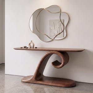 Puede incluir: Una mesa consola de madera oscura con una base curva en forma de onda y una superficie superior plana. Sobre la mesa cuelga un espejo de pared irregular de varias secciones con un marco dorado fino. Una pequeña escultura de cerámica color crema.