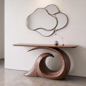 Puede incluir: Una mesa consola de madera oscura con una base curva en forma de ola y una superficie plana. Sobre la mesa hay una pequeña esfera plateada y una lámpara de metal delgada. Sobre la mesa cuelga un gran espejo de pared irregular con marco.