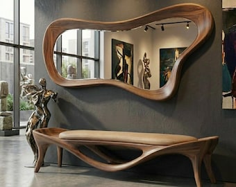 May include: A wooden bench with a smooth, curved, organic frame and a light-colored upholstered seat, paired with a large, matching wall-mounted mirror featuring an irregular, flowing wooden border that reflects the surrounding room.