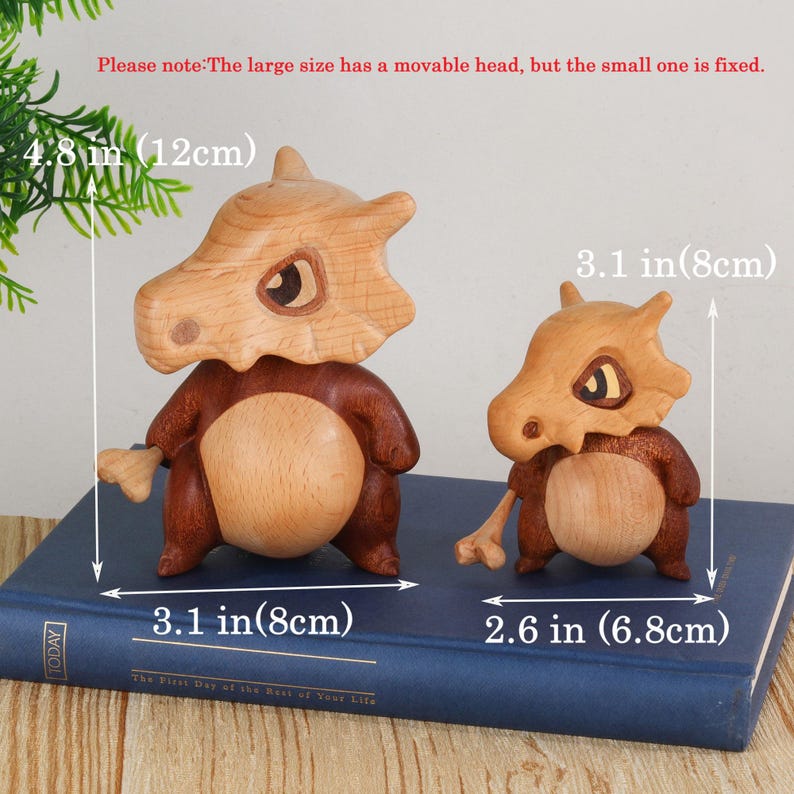 Puede incluir: Dos figuras de madera, una grande y otra peque&ntilde;a, que se asemejan a una criatura parecida a un dinosaurio. La figura m&aacute;s grande mide 12 cm de alto y 8 cm de ancho, mientras que la m&aacute;s peque&ntilde;a mide 8 cm de alto y 6,8 cm de ancho. El texto de la imagen dice "The First Day of the Rest of Your Life."