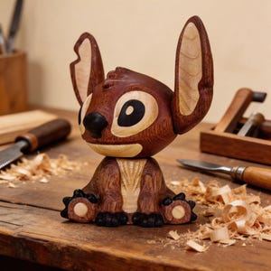 May include: A handcrafted wooden figurine of a cartoon character with large ears, a black nose, and large eyes. The figure is made of dark and light brown wood, with visible wood grain. The figurine is sitting on a wooden surface, with wood shavings and tools in the background.
