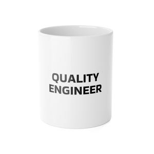 May include: A white ceramic mug featuring the text QUALITY ENGINEER printed in bold black capital letters on the front. The mug has a cylindrical shape with a smooth finish and a wide opening at the top, displaying a clean and simple design.