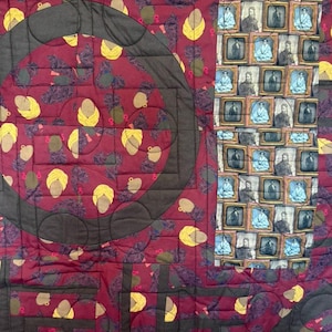 May include: A handmade quilt with a complex pattern. The quilt features a deep red background with repeating shapes, including circles and rectangles. There are also repeating images of people in small frames. The quilt is stitched with dark gray thread.
