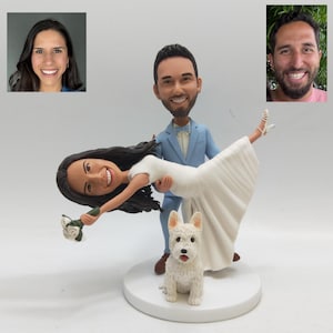Puede incluir: Una figura para pastel de bodas que representa a una pareja bailando, con un perro blanco pequeño. El novio lleva un traje azul claro y la novia un vestido blanco. La figura está sobre una base circular blanca.