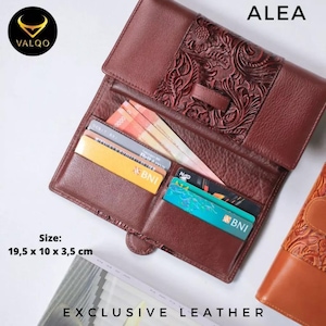May include: A brown leather wallet with an embossed floral design, open to reveal card slots and cash. The wallet is labeled "ALEA" and "EXCLUSIVE LEATHER." Dimensions are 19.5 x 10 x 3.5 cm.