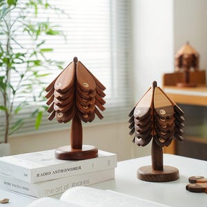 Pode incluir: Duas esculturas decorativas de árvores de madeira com um design de peixe. As árvores são feitas de madeira marrom escura e têm um design em camadas. Elas ficam em bases redondas e são exibidas em uma superfície branca com livros.