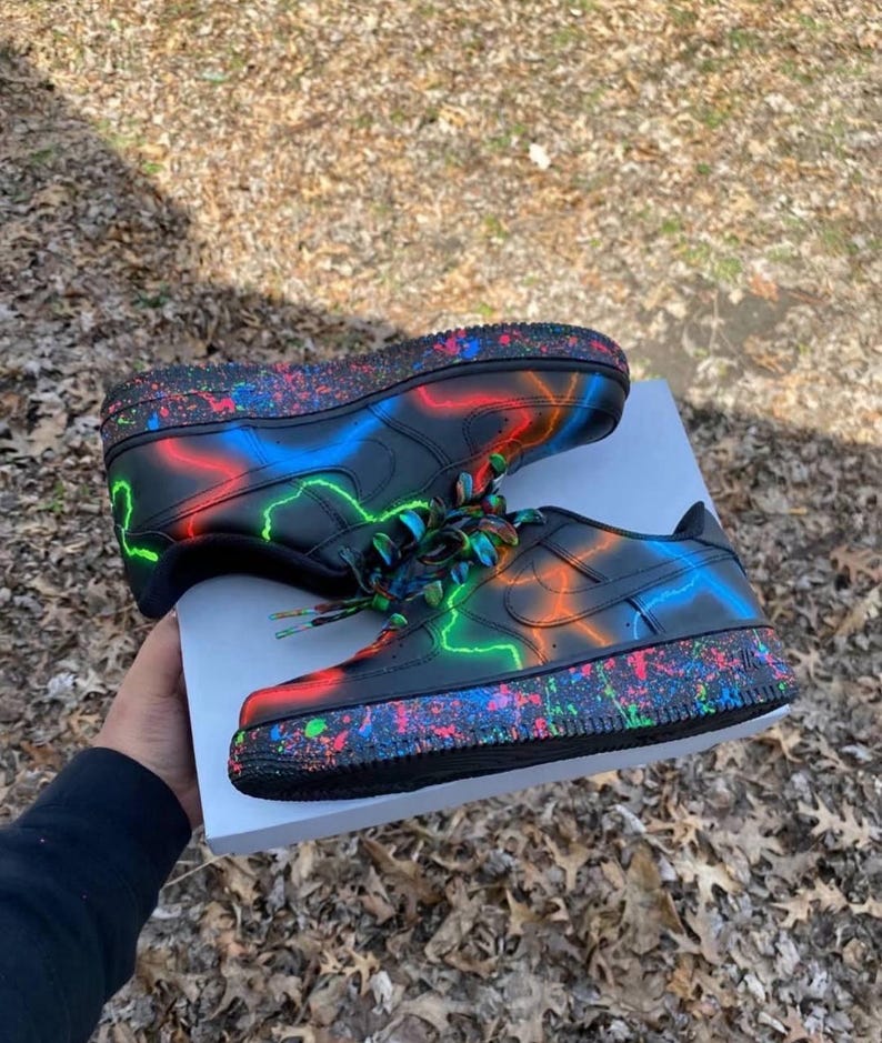 Pu&ograve; includere: Scarpe da ginnastica nere con fulmini al neon rossi, blu e verdi. Le suole hanno un effetto vernice a spruzzo colorato. I lacci sono multicolore.