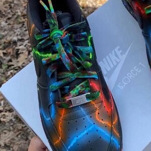 Pu&ograve; includere: Scarpe da ginnastica Nike Air Force 1 nere con accenti neon colorati. Le scarpe presentano una base nera con vivaci disegni blu, arancioni e verdi. I lacci sono multicolori e la linguetta mostra il logo Nike. Su una scatola bianca.